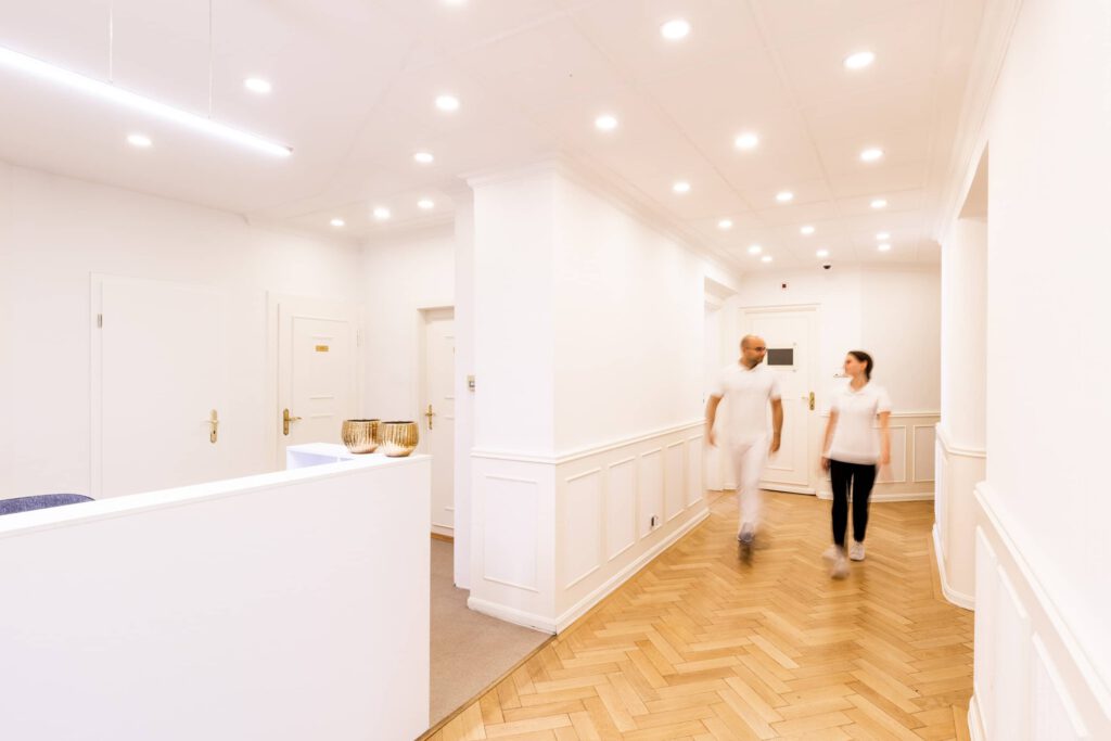 Fotografie einer Praxis im Empfangsbereich, Zwei Mitarbeiter gehen durch den Gang