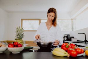 Content Fotoproduktion für eigenes Label, Frau steht in der Küche mit Obst und Gemüse im Vordergrund